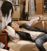 a man is laying on a couch in a living room with a woman standing behind him .