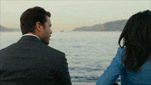 a man in a suit and a woman in a blue shirt are looking out over the water
