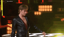 a man in a black leather jacket stands on a checkered dance floor with the words voz en directo on the bottom left