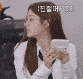 a woman wearing glasses and a white shirt holds a cell phone with the number 33 above her