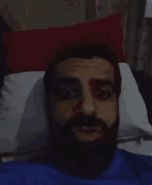 a man with a beard is laying in a bed with a pillow .