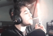 a man wearing headphones is smoking a cigarette in a dark room .
