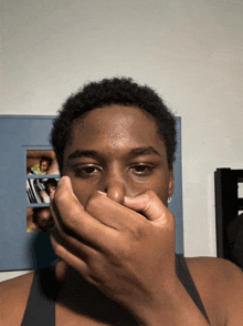 a man covering his mouth with his hand in front of a wall with pictures