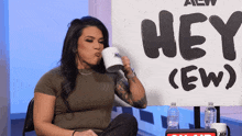 a woman drinking from a cup in front of a sign that says hey ( ew )