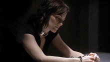 a woman wearing handcuffs and a collar looks down at something