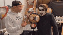 a man wearing a state champ sweatshirt talks to a man holding a wrestling championship belt