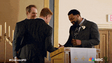 a man in a suit shakes hands with another man at a podium with nbc written on the bottom right