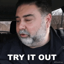 a man with a beard is sitting in a car and says try it out