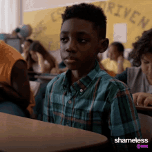 a boy in a plaid shirt sits at a desk in front of a sign that says rivera