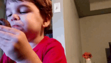 a young boy in a red shirt is eating a donut in a living room .