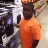 a young man in an orange shirt is standing in front of a playstation 4 display in a store .