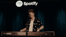 a man is singing into a korg keyboard in front of a spotify logo