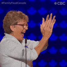 a woman applauds in front of a microphone with the words family feud canada on the bottom