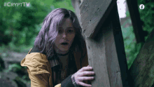 a girl with purple hair is standing next to a wooden post with the crypttv logo on the bottom