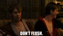two men are sitting on a couch and one of them is saying `` don t flush '' .