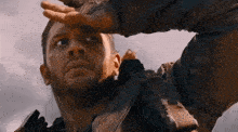 a man in a leather jacket is looking up at the sky with his hand on his forehead .