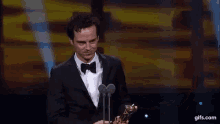a man in a tuxedo is holding a trophy in front of a microphone .