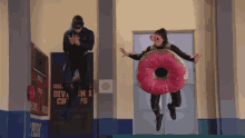 a woman in a donut costume is jumping in the air while a man watches