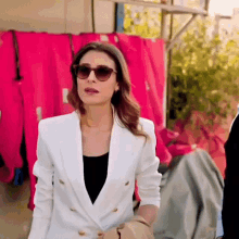 a woman wearing sunglasses and a white jacket is standing in front of pink clothes