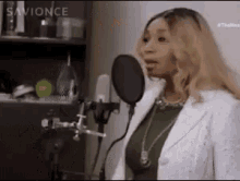 a woman in a white jacket is singing into a microphone in a recording studio .