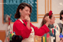 a woman in a red sweater and white apron is laughing and making a fist .