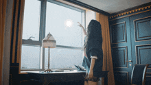a woman stands in front of a large window looking out
