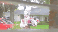 a man in a british costume is holding a camera in front of a red car
