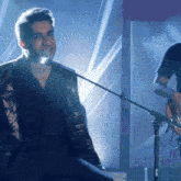 a man singing into a microphone while another man plays guitar