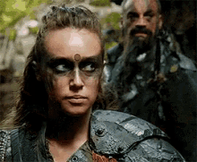a woman with face paint and a man with a beard are standing next to each other in the woods .
