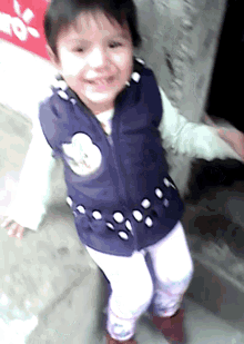 a little girl wearing a blue vest and white pants smiles