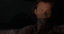 a man is sitting in a car at night with his eyes glowing .
