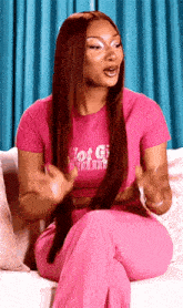 a woman in a pink shirt and pink pants is sitting on a couch talking to someone .