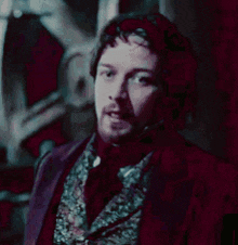 a man with a beard is wearing a purple suit and a purple vest .