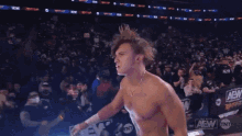 a shirtless wrestler stands in front of a crowd with aew written on the bottom
