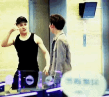 a man in a black tank top talks to another man in a grey jacket