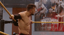 a man in a wrestling ring with a poster for wrestlemania behind him