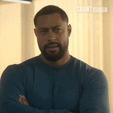 a man with a beard is standing with his arms crossed in front of a curtain that says countdown