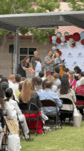 a group of people are sitting in chairs under a canopy while a man holds a microphone