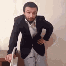 a man in a suit is standing with his hands on his hips and holding a laptop .