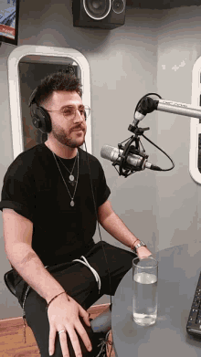 a man wearing headphones sits in front of a microphone with a glass of water on the table
