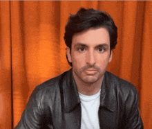 a man wearing a black leather jacket and a white shirt looks at the camera