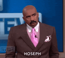 a man in a suit and tie is standing in front of a blue wall and says hoseph .