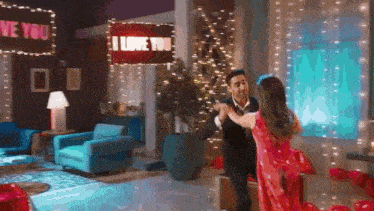 a man and woman are dancing in a living room with a sign that says i love you .