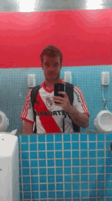 a man in a river plate jersey takes a picture of himself in a bathroom mirror