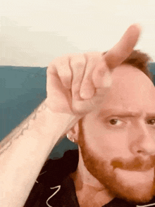 a man with a beard is making a funny face with his finger on his forehead .