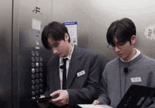 two men are in an elevator with the letter f on the wall behind them