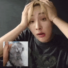 a man is holding his head in his hands while looking at a picture of a cat .