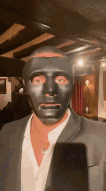 a man wearing a black mask and a suit stands in a dark room