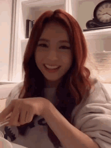 a woman with red hair is smiling in front of a clock on a shelf