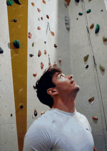 a man in a white shirt is looking up at a climbing wall with princemick written on the bottom